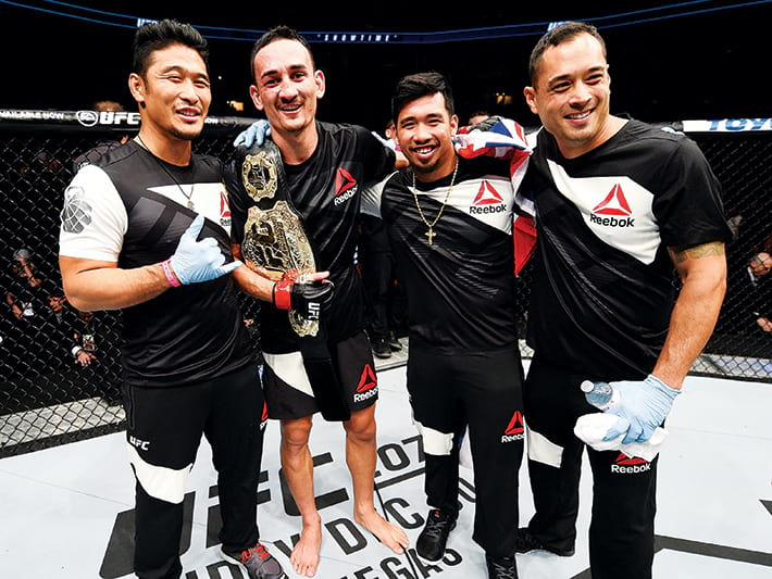 max holloway holding belt with his team in the octagon